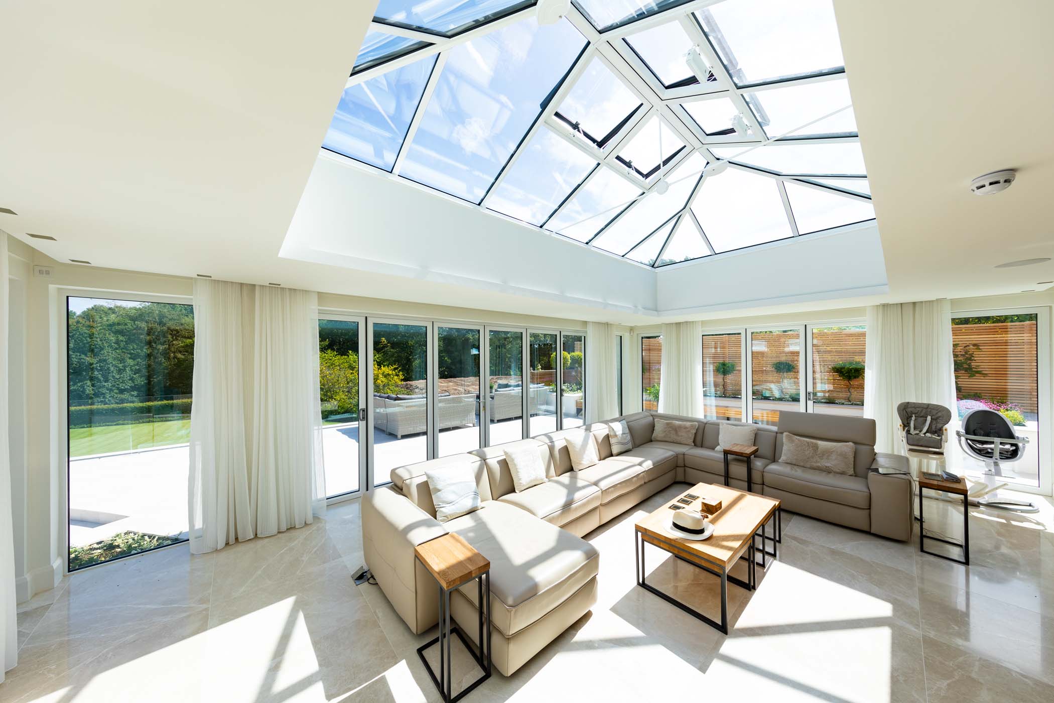 a living area with large glass and aluminium windows with a sloped glazed roof